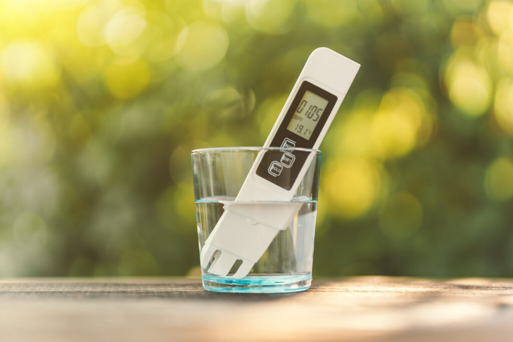 tds measurement of water. electronic ph meter in a glass of water. poor water quality, high values of salt impurities, blurred background of nature